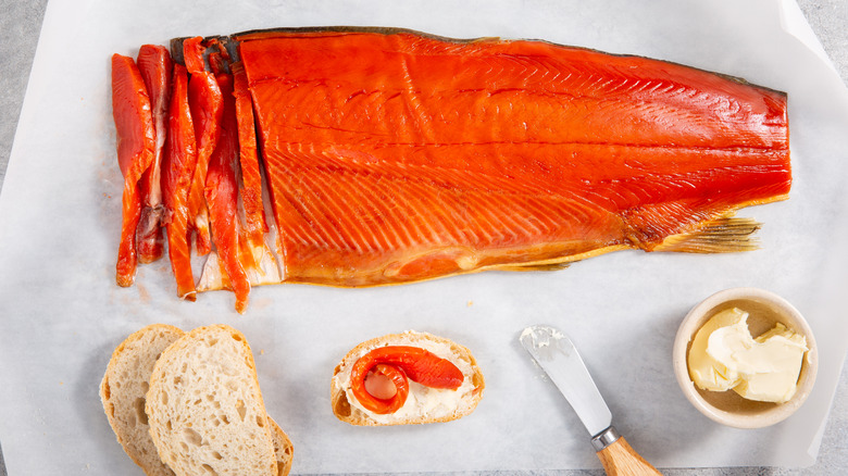 Cold-smoked sockeye salmon partially sliced with slices of bread and butter on parchment paper.