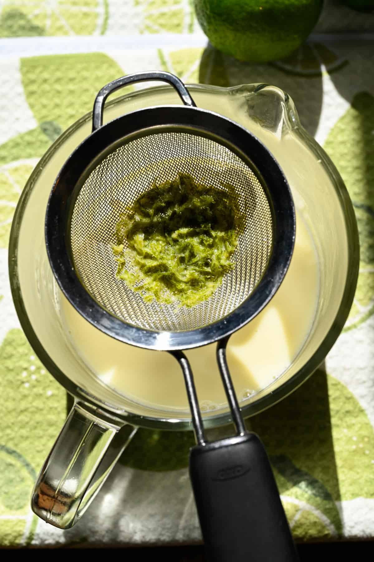 Lime zest in a small strainer over a pot of hot cream.