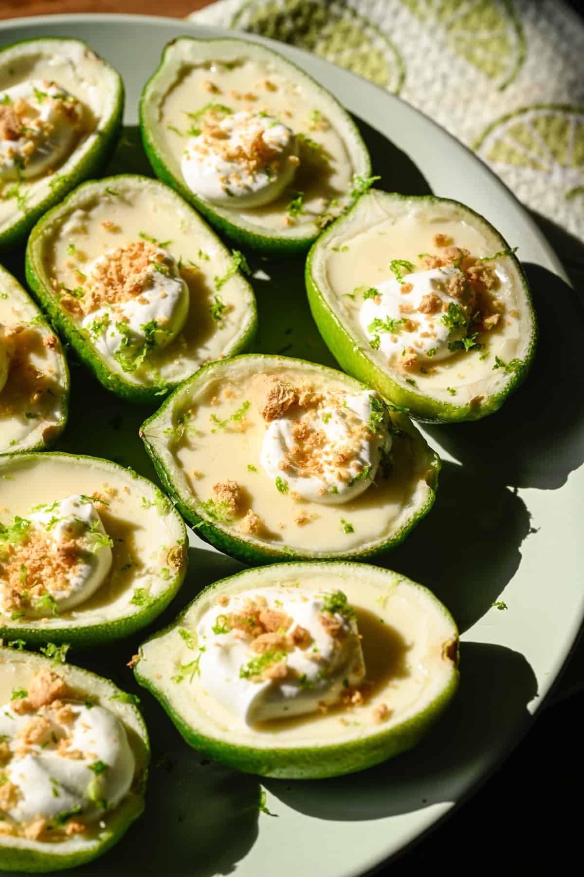 Close up view of lime possets topped with whipped cream and graham cracker crumbs on light green plate. 