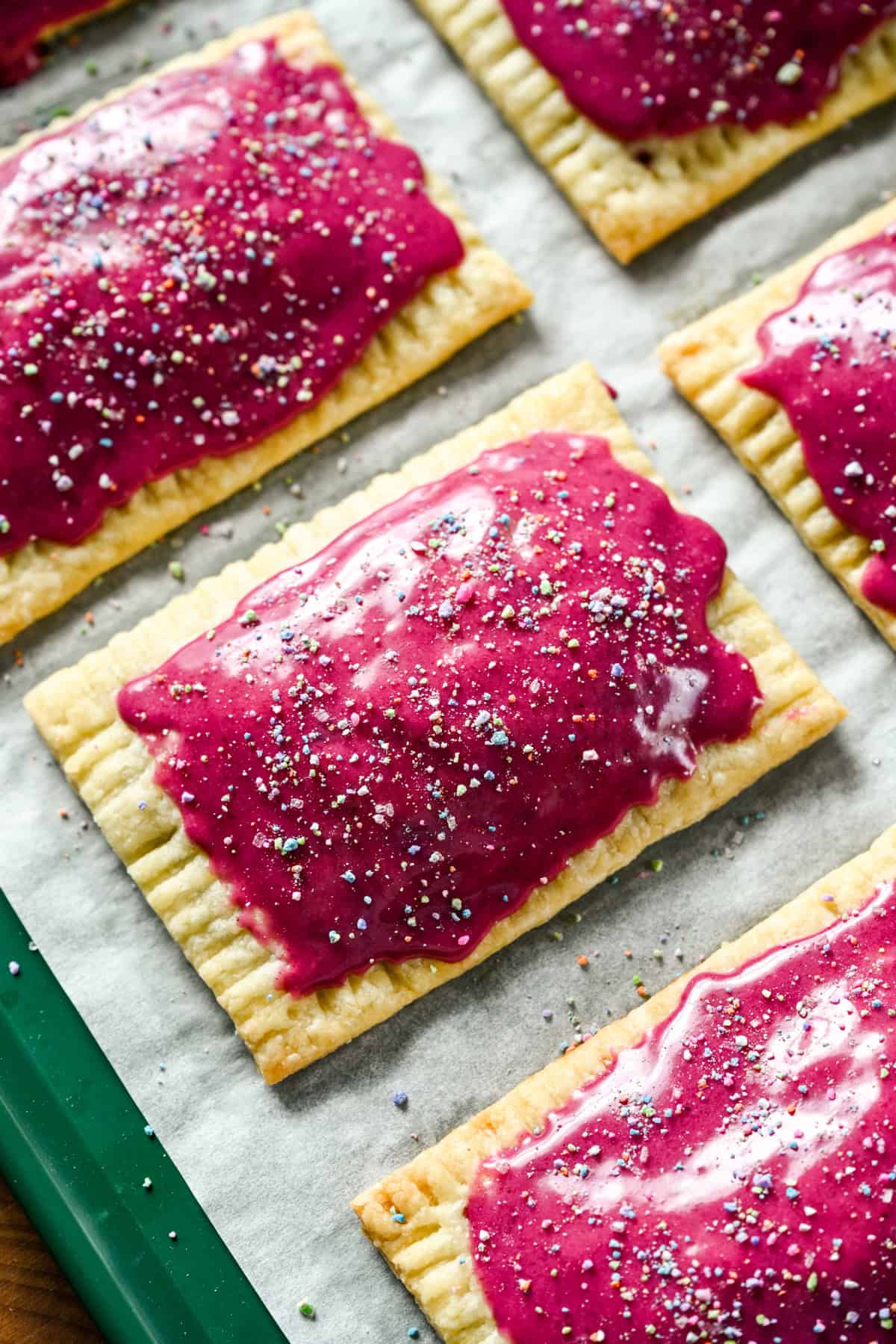 close up view of homemade blueberry pop tarts with bright pink icing and sprinkles on a sheet pan.