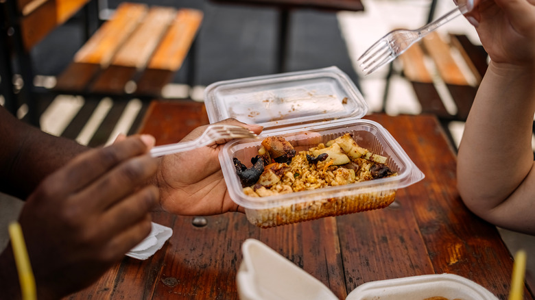 Food packed in a plastic container between two hands holding forks