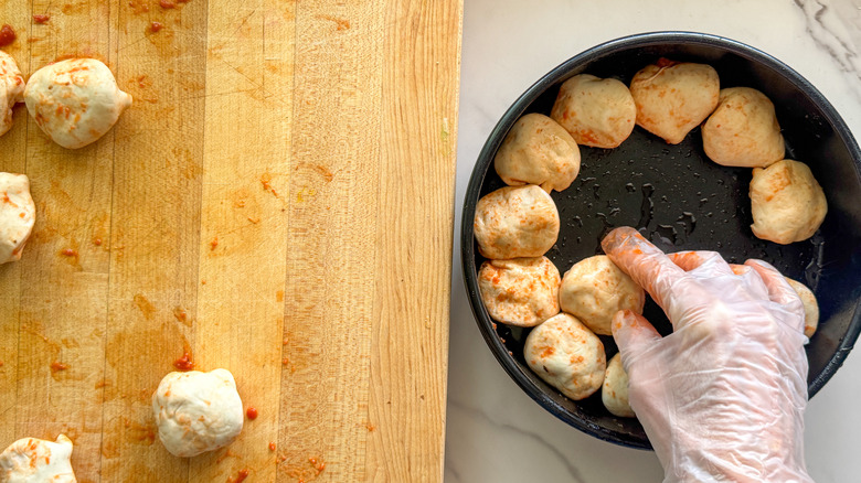 hand adding sauce to dough squares