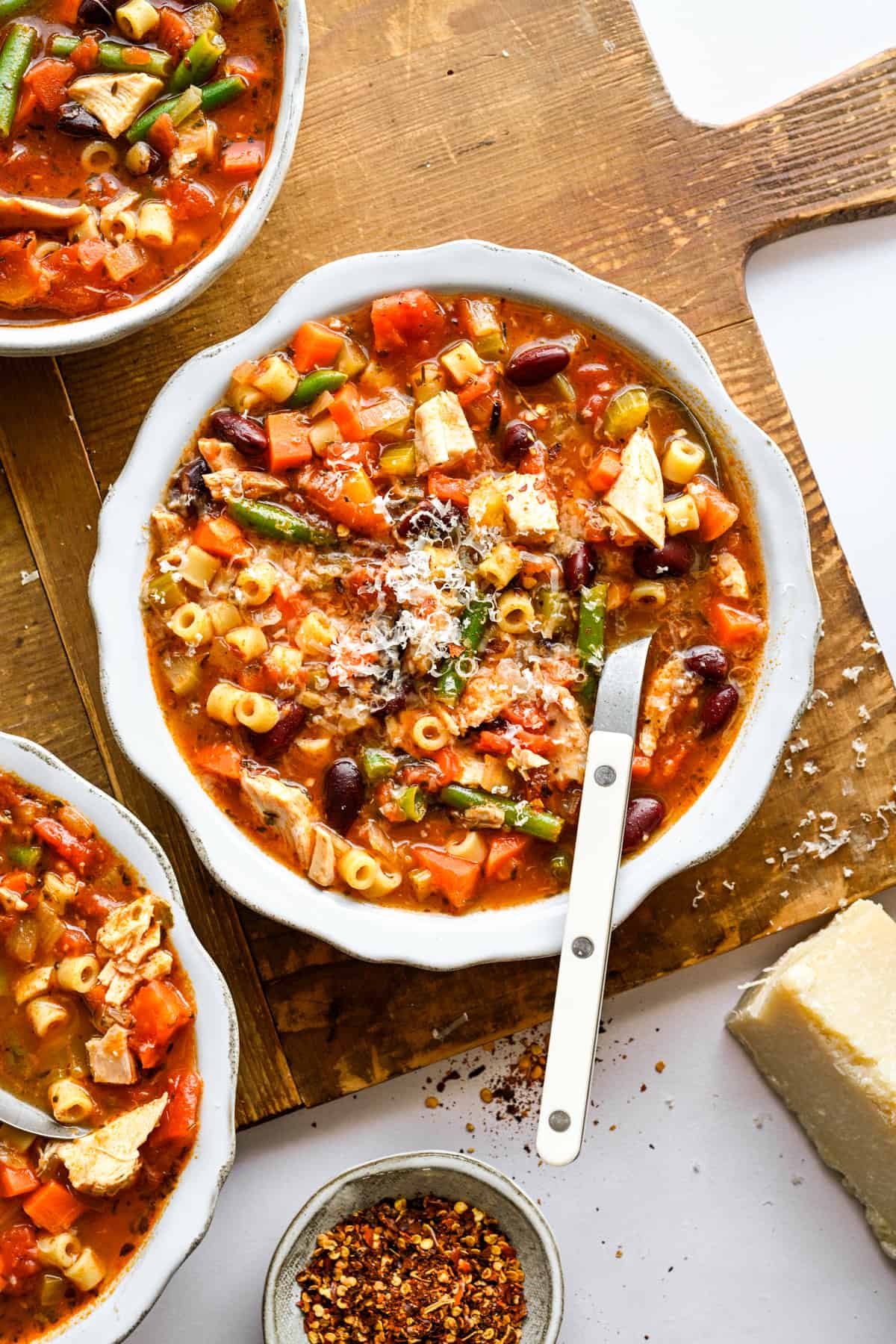 Chicken Minestrone Soup with a soup spoon, topped with fresh parmesan cheese.