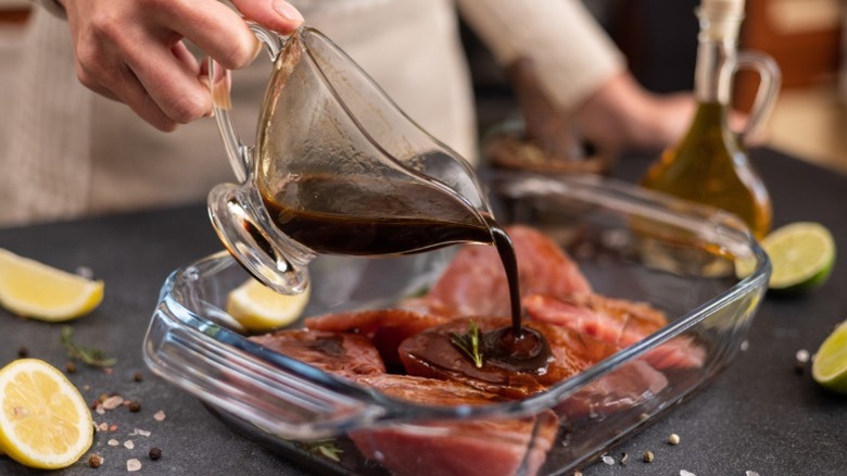 A chef pouring a whiskey marinade over cuts of steak with in a baking dish.