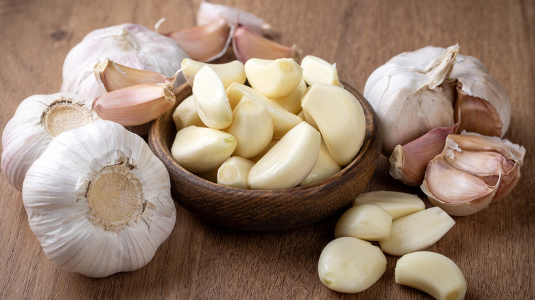 Whole unpeeled garlic bulbs surrounding a small wooden bowl of peeled garlic cloves.