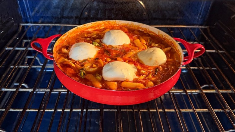 Spicy tteokbokki with burrata baking in red pan in oven