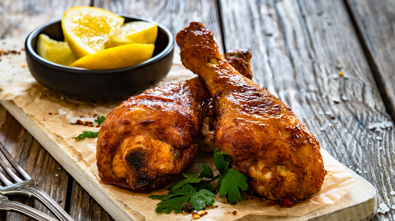 Air fryer chicken drumsticks served with lemon wedges in a small black bowl on a small wood platter on top of wood table.