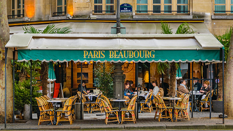 The exterior of a French cafe, with a teal awning that reads 