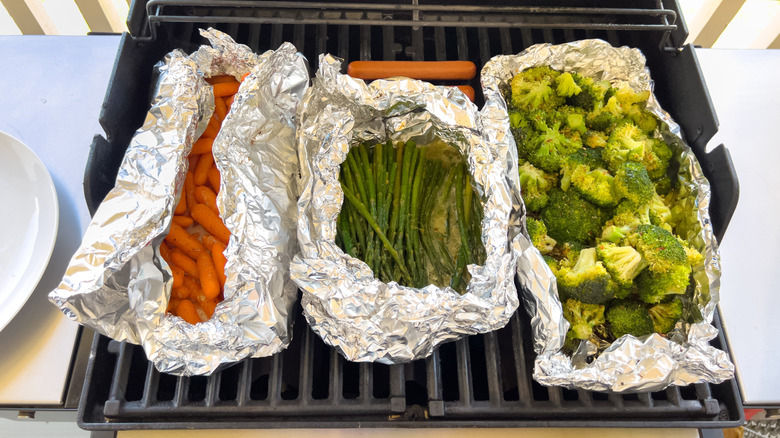 Foil packets of carrots, asparagus, and broccoli on a grill