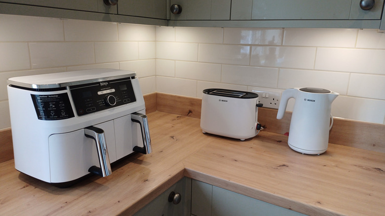 An air fryer on a counter top by a toaster and electric kettle