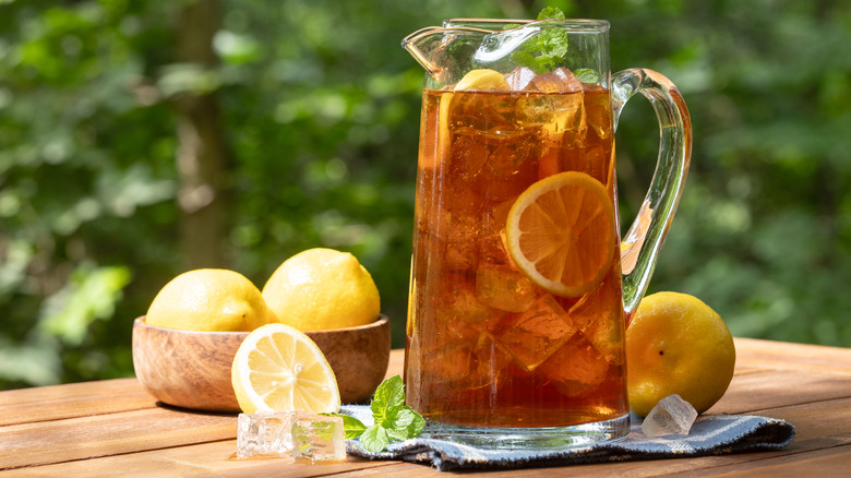 A pitcher of black iced tea surrounded by lemons.