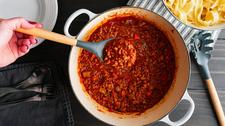 Ragu alla bolognese Italian tomato and meat sauce in a spoon held over a large Dutch oven pot.