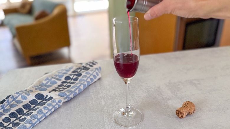 Pouring blood orange juice into a champagne flute with mixed berry syrup