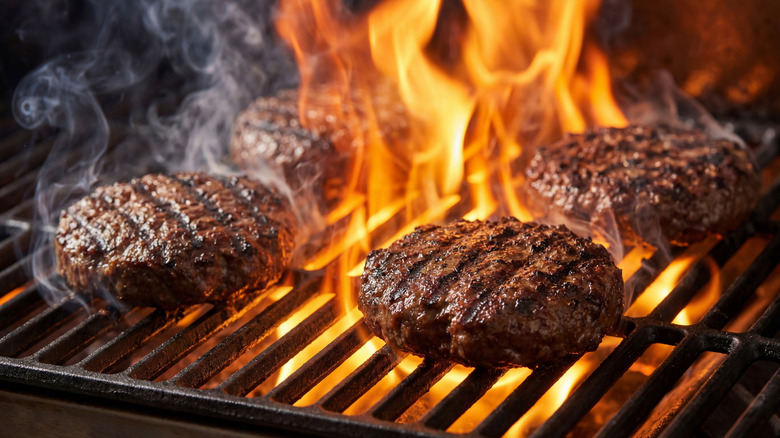 Thick patties on a grill being cooked over flame