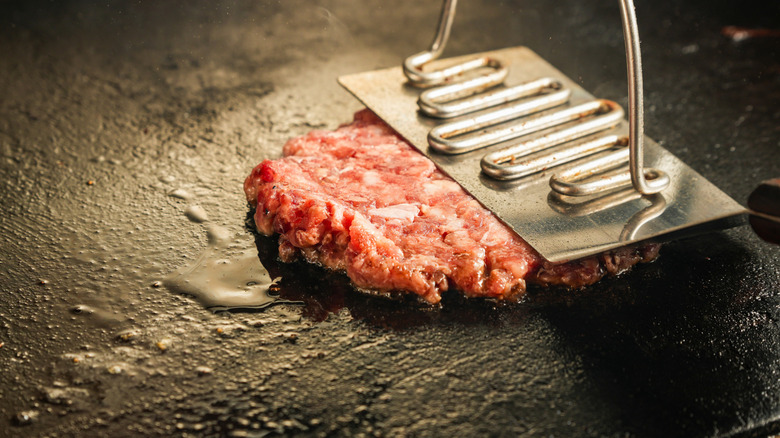 Meat on a griddle being pressed down.