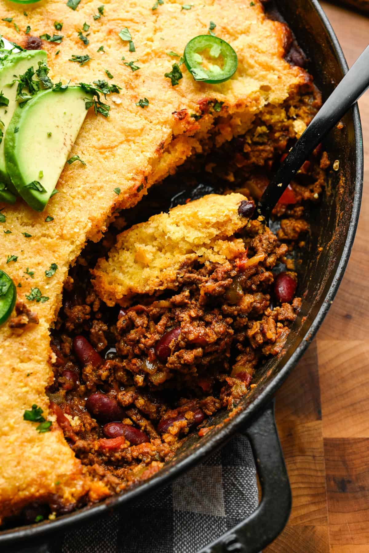 A spoon scooping out chili pie from the skillet.