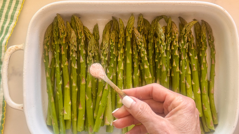 hand adding salt to asparagus