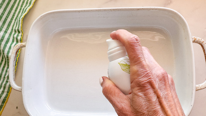 hand spraying the baking dish