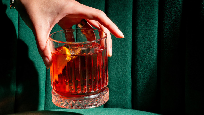 Hand holding a negroni cocktail with an orange slice in it