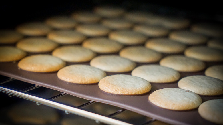 Rows of cookies baking in an oven on a silicone baking mat.