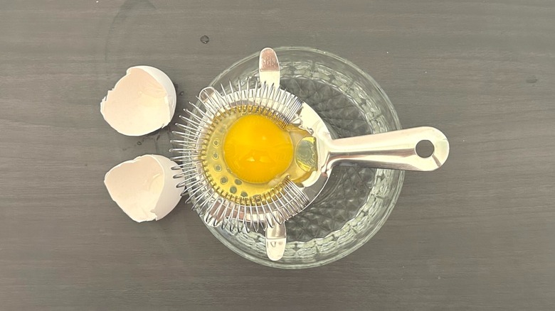 Egg strainer over a bowl with an egg cracked on top of it