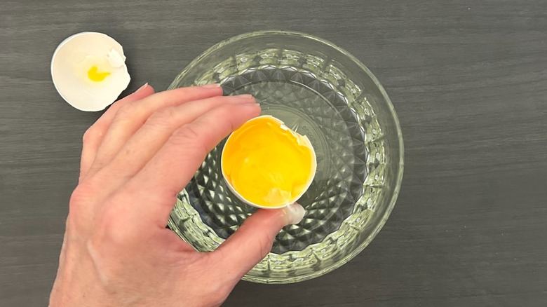 Hand holding an egg shell with yolk in it over a bowl full of egg whites