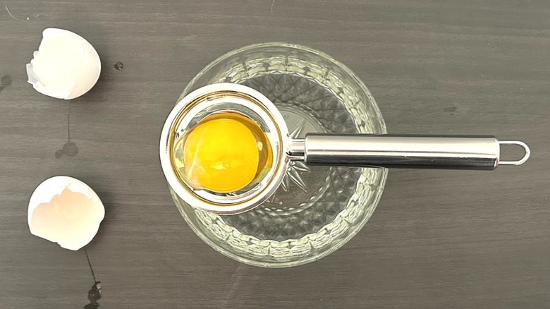 Egg cracked into a metal egg separator placed over a glass bowl