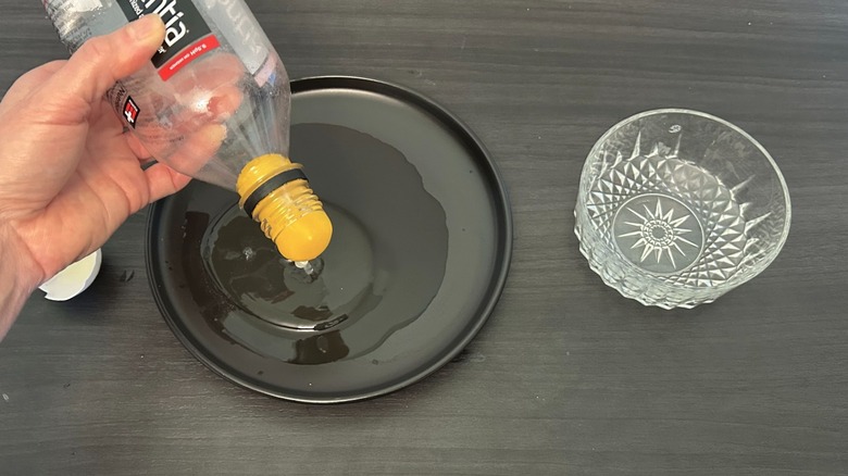 Egg yolk being sucked up by a plastic bottle over a black plate next to a glass bowl