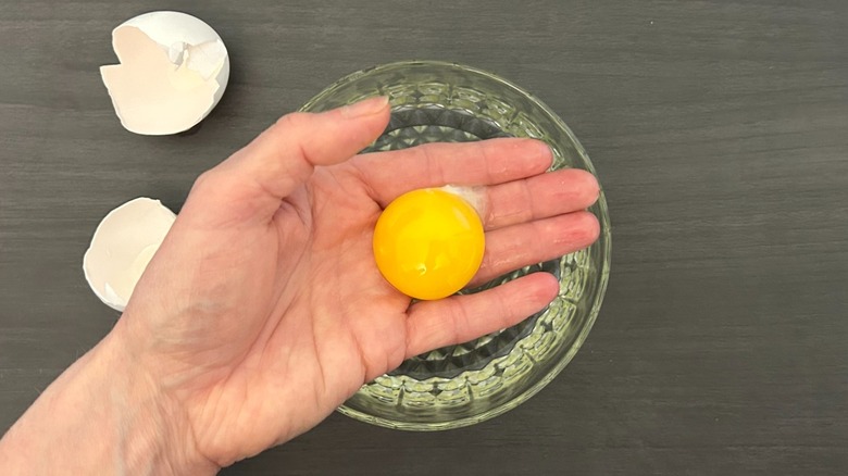 Hand holding an egg yolk over a glass bowl filled with whites