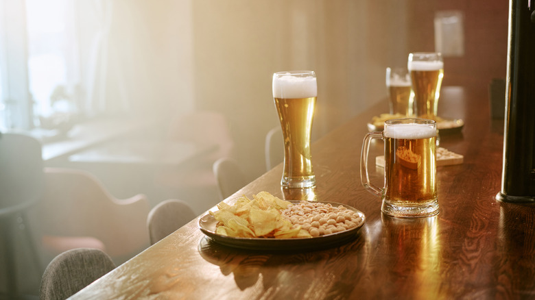 A saloon bar with several glasses of beer and a plate of chips and peanuts