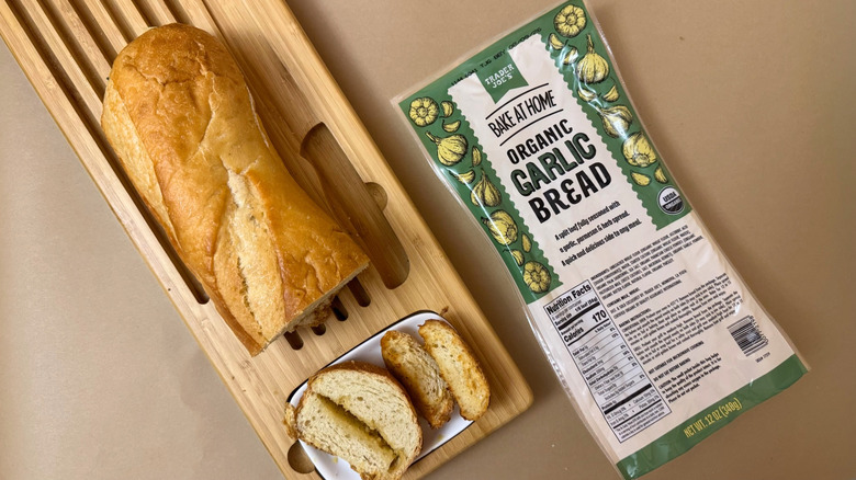 Loaf of Trader Joe's Organic Garlic Bread on wooden board beside product packaging