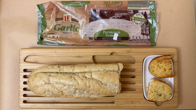 Loaf of L'Oven Fresh Parmesan Romano Garlic Bread on wooden board beside product packaging
