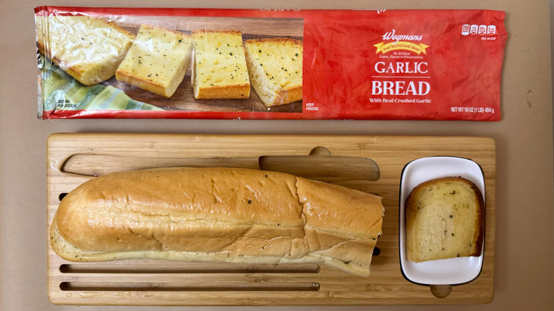 Loaf of Wegman's Frozen Garlic Bread on wooden board beside product packaging