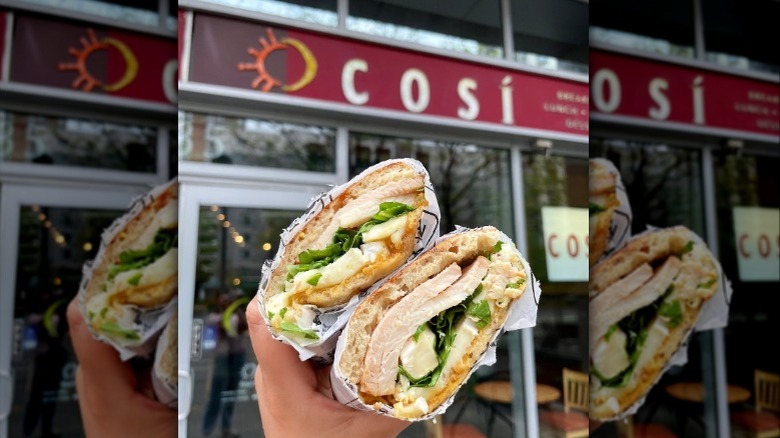A person holding a sandwich in front of the Cosi sign