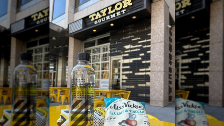 Bottle of water, chips, and sandwich on a table in front of Taylor Gourmet