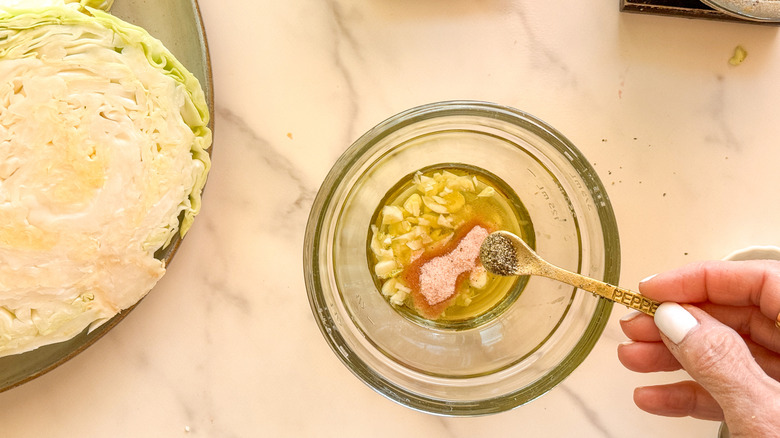 hand adding pepper to bowl with oil and garlic