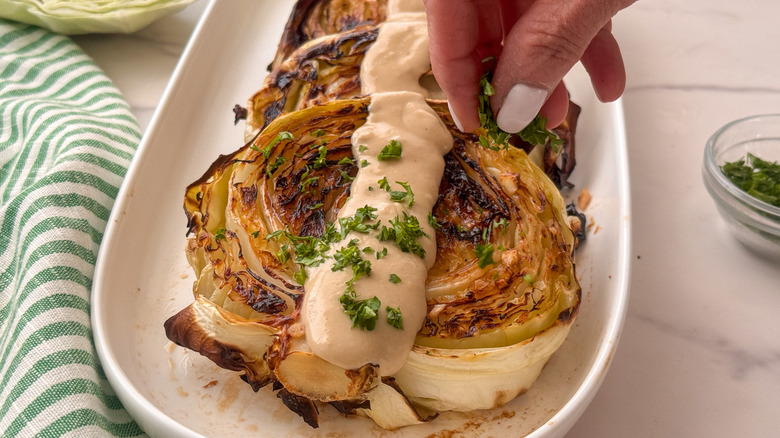 hand sprinkling parsley onto roasted cabbage with tahini sauce