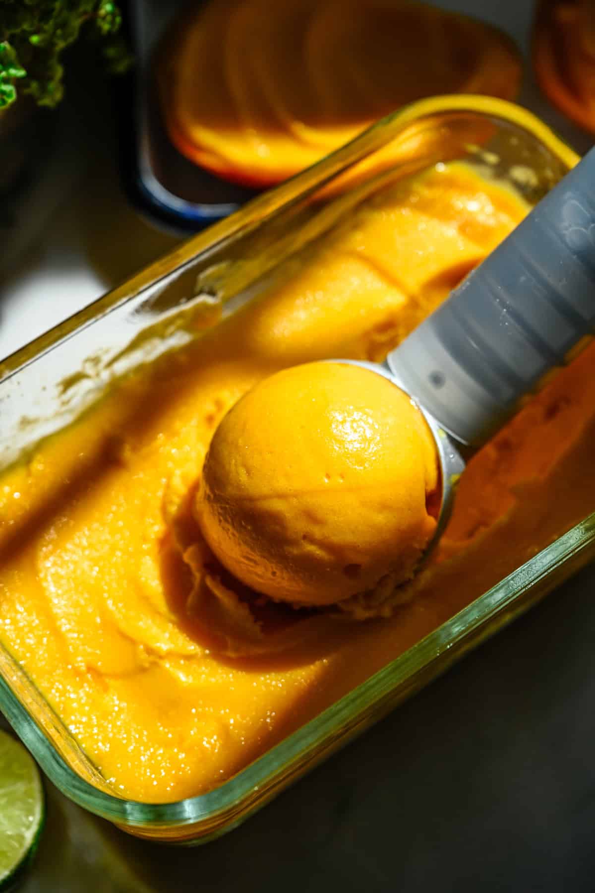Close up view of a scoop of mango sorbet sitting in a container of sorbet.