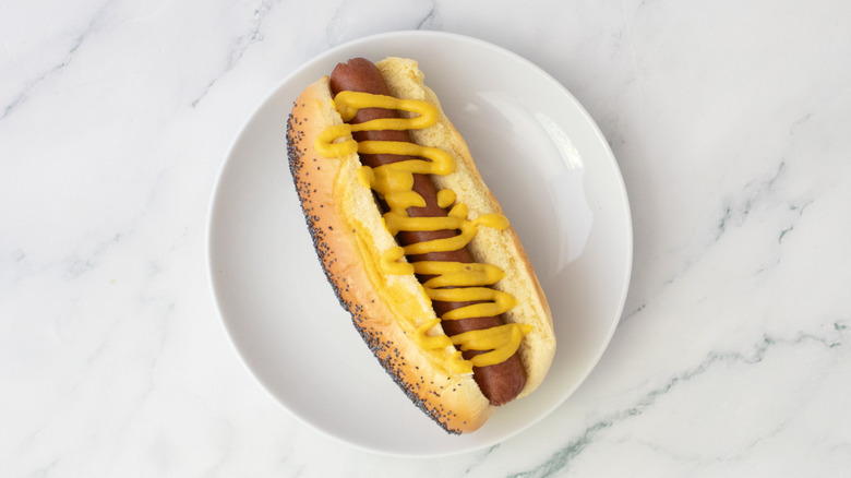 Hot dog in a bun, drizzled with mustard on a white plate