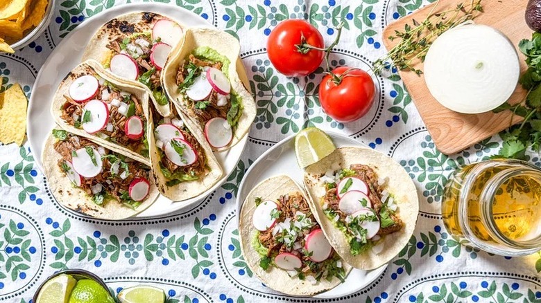 two plates of Slow Cooker Barbacoa Tacos on a patterned tablecloth