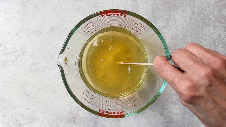 Stirring brown sugar and water in a glass measuring cup with wooden spoon