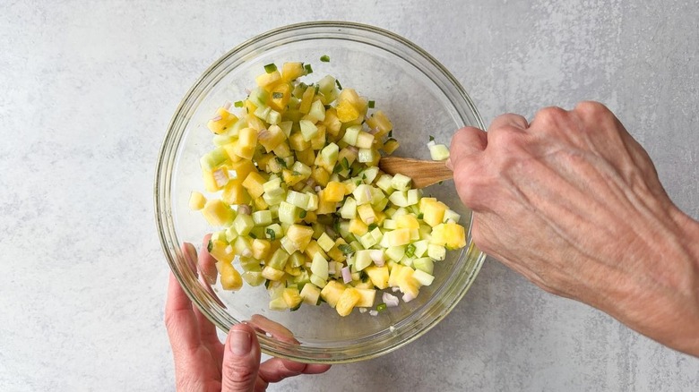 Mixing cucumber and pineapple relish in glass bowl with wooden spoon