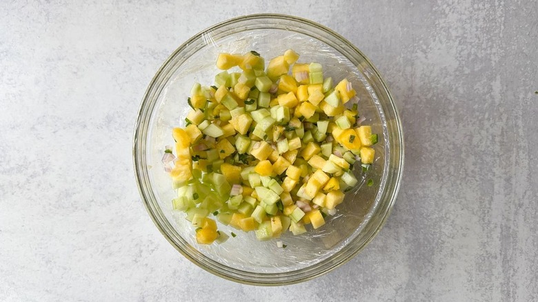 Cucumber and pineapple relish in glass bowl covered with plastic wrap
