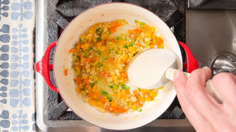 Stirring sambal vegetables cooking in coconut oil in red pot on stovetop