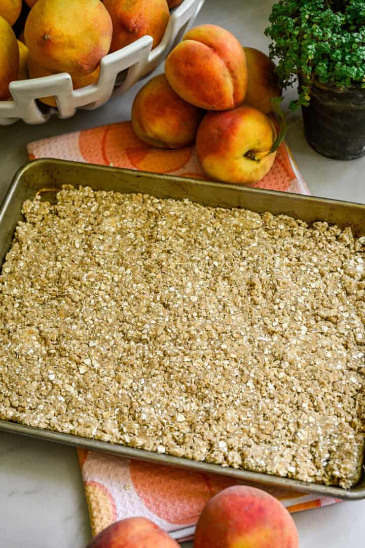 Overhead view of peach crisp pushed into a rimmed baking sheet.