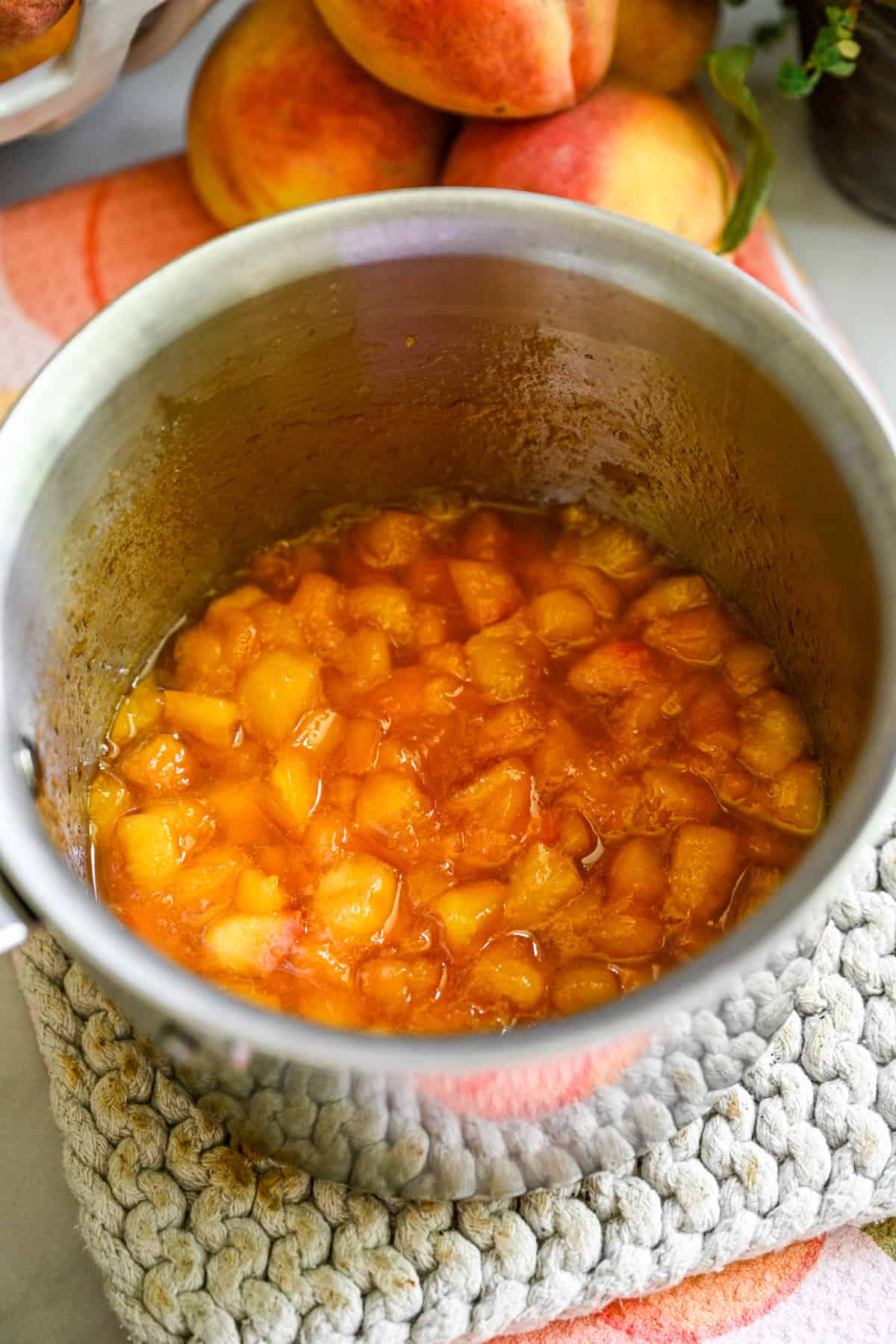 Overhead view of peach compote in a stainless steel saucepan.
