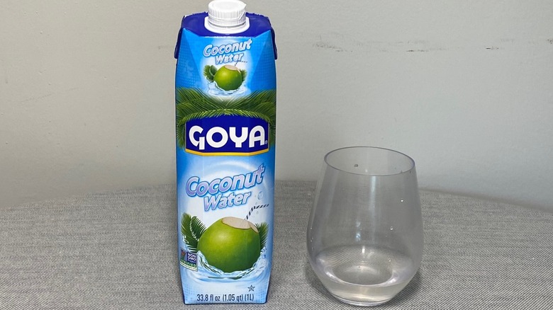 A carton of Goya coconut water on a table beside a glass of the product