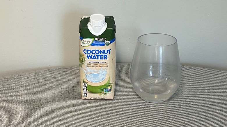 A carton of Simply Nature coconut water on a table beside a glass of the product