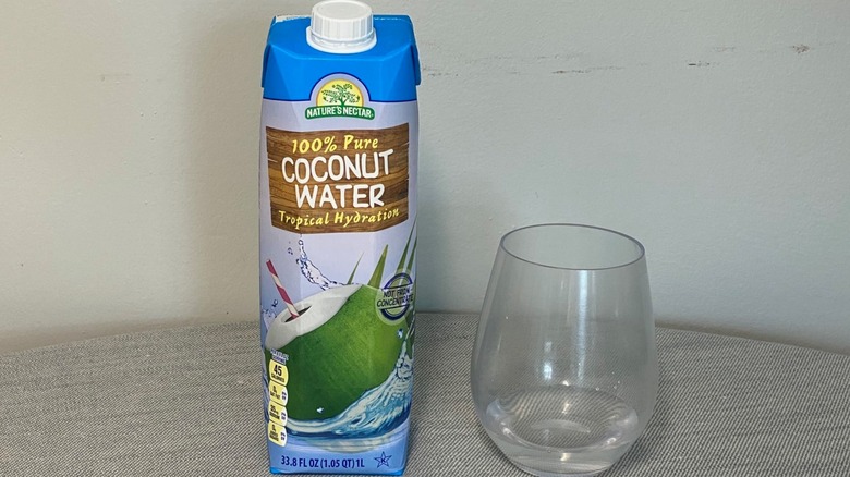 A carton of Nature's Nectar coconut water on a table beside a glass of the product