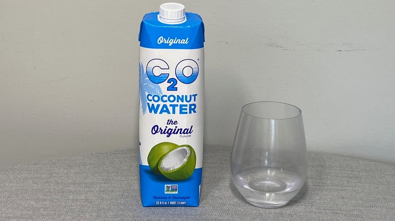 A carton of C2O Coconut Water on a table beside a glass of the product